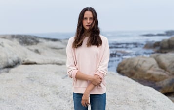 En flicka i rosa tröja på klippor vid havet